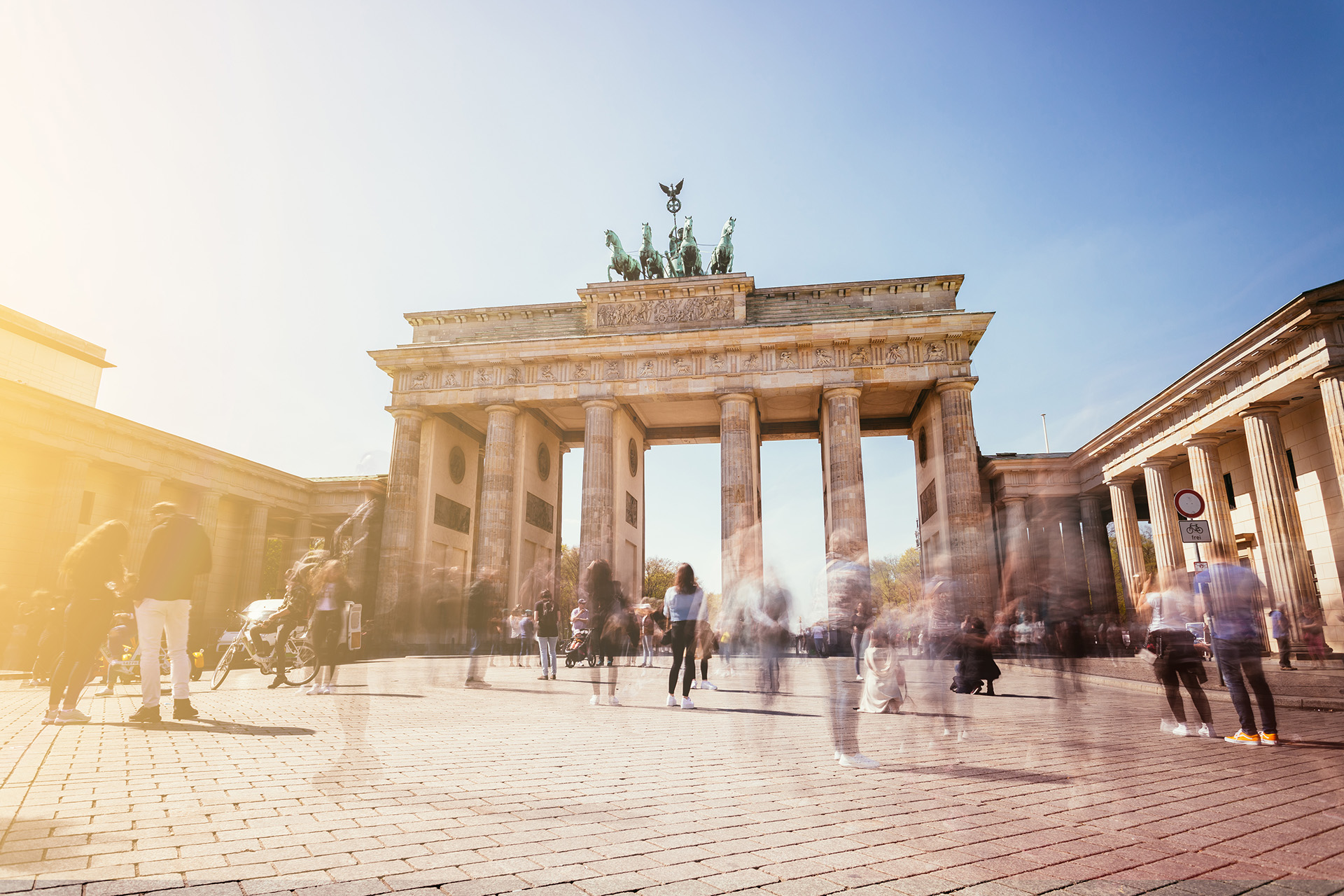 Brandenburger Tor vor unbewölktem Himmel mit Menschen im Vordergrund.